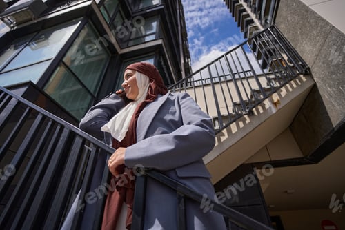 Preview: Arab woman stands on ladder against the background of high-rise building and sky