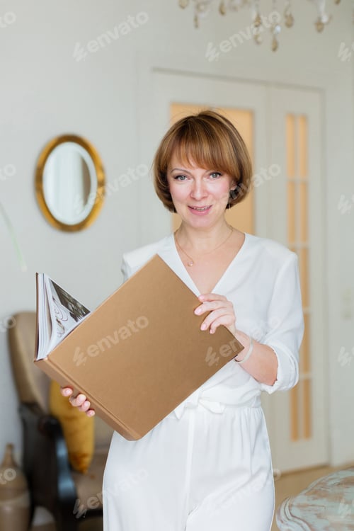 Preview: An adult beautiful woman spends time in her stylish living room and holds a big book in her hands.