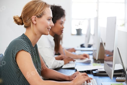Preview: Young woman working at computer in office beside colleagues
