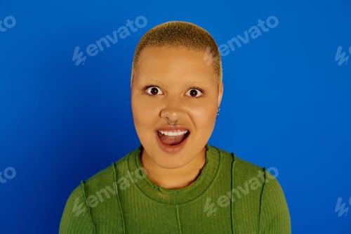 Preview: Young stylish woman joyfully expressing herself in a vibrant blue setting during a creative shoot