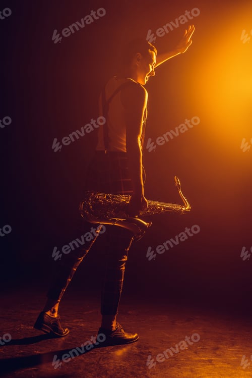 Preview: smiling young saxophonist holding saxophone and waving hand