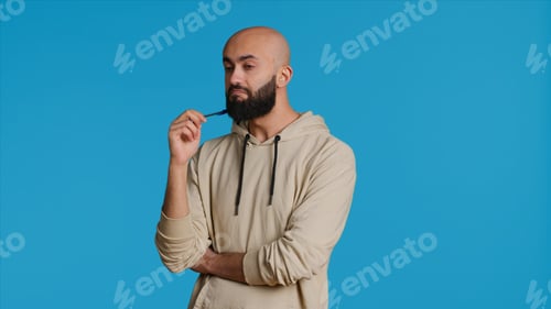 Preview: Thoughtful Man in Hoodie with Pen Against Blue