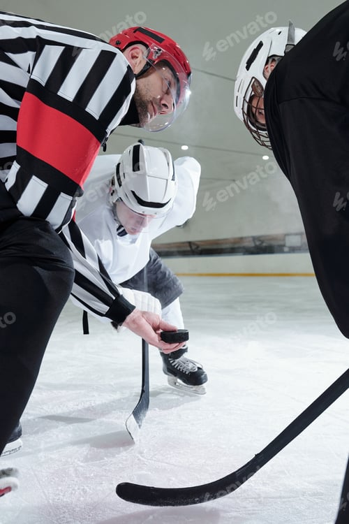Preview: Hockey referee with puck looking at one of two players bending forwards