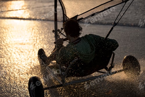 Preview: Rear view of person riding a sand yacht along a sandy beach at sunset.