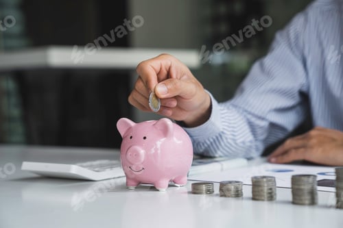 Preview: Businessman with a coin in a piggy bank along with pressing the calculator and writing down savings
