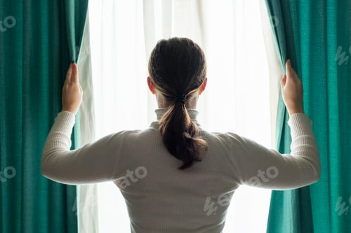 Preview: Woman stands at window and opens curtains rear view.