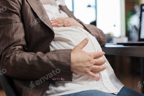Preview: Close up of pregnant woman touching baby bump while in company office workplace.