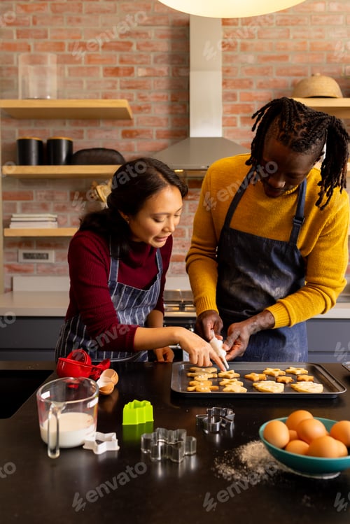 Preview: Happy diverse couple in aprons decorating christmas cookies in kitchen, copy space