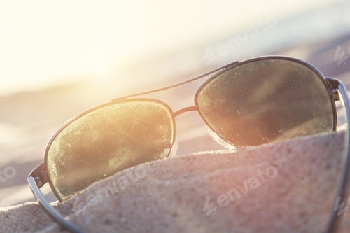Preview: Sunglasses on sand at sunset, beach and ocean in the background.