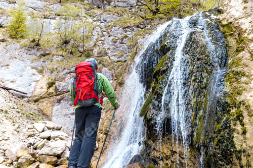 Preview: Hiker with a red backpack observes a waterfall