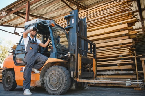 Preview: Warehouse worker driving forklift by lumber stacks