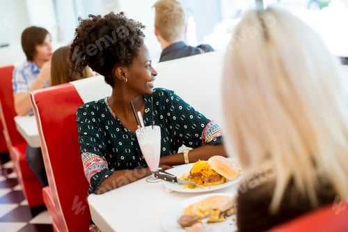 Preview: Multiracial female friends eating fast food at a table in the diner