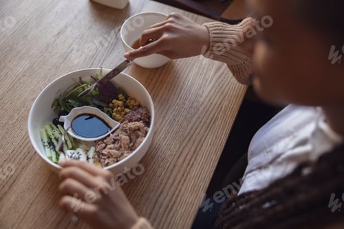 Preview: Top view of woman holding cutlery and eating healthy food served in white ceramic bowl
