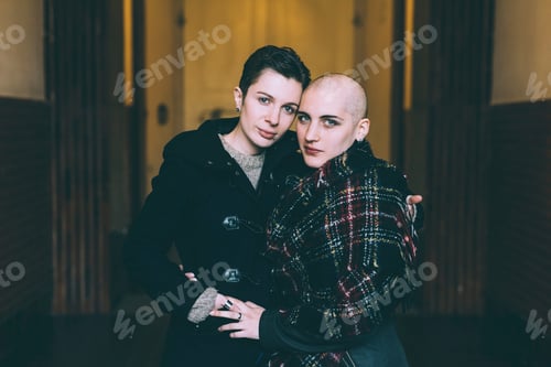 Preview: Portrait of young lesbian couple with arms around each other in hallway