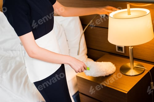 Preview: cropped view of housemaid in white apron holding duster and cleaning hotel room
