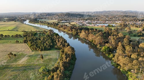 Preview: Aerial view of a river flowing through green countryside with a town in the background.