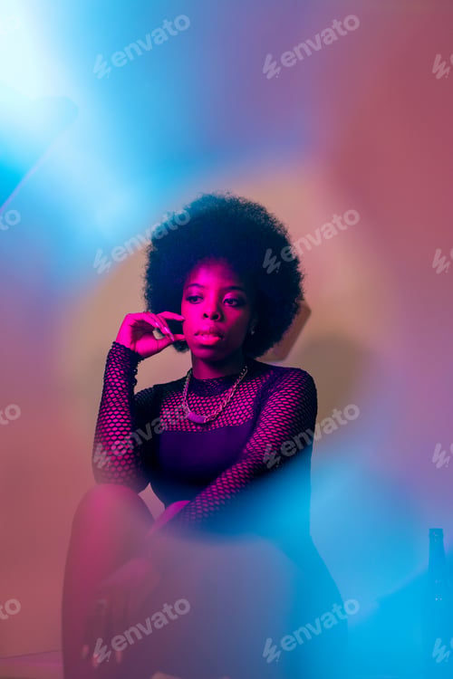 Preview: Pretty young woman of African ethnicity in elegant black dress sitting by wall