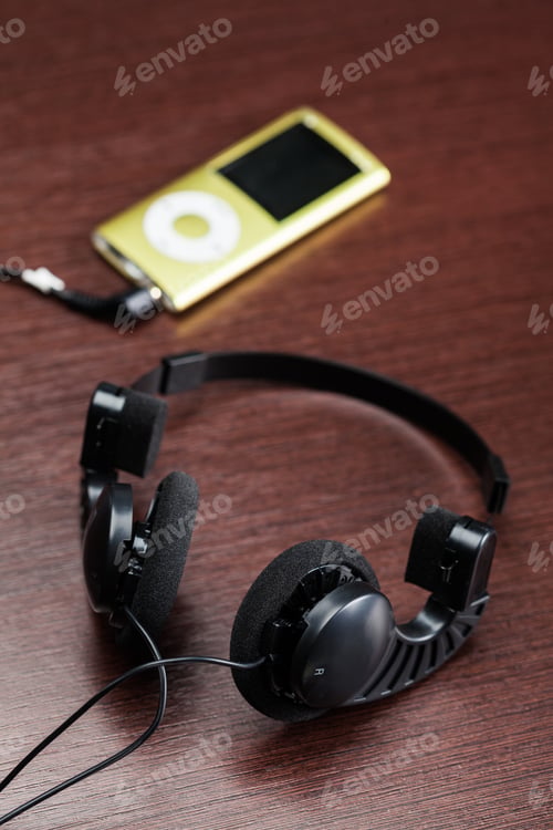 Preview: Headphones and music player sit on a wooden table in a casual space at midday
