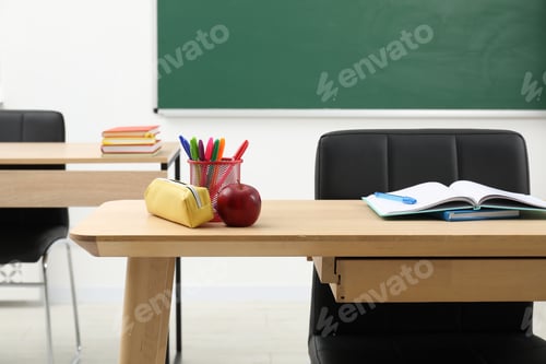 Preview: Different school stationery and red apple on wooden table near blackboard indoors