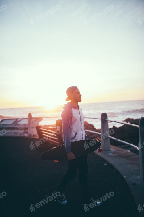 Preview: Young adult man walking on promenade with longboard
