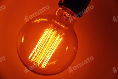 Preview: Vintage light bulb on orange background, closeup. Glowing edison bulb