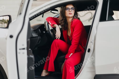 Preview: beautiful sexy rich business woman in red suit sitting in white car, wearing glasses
