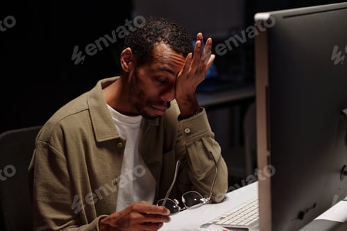 Preview: Tired African American Man Rubbing Eyes at Desk