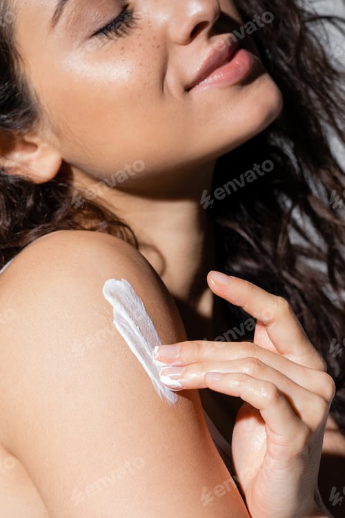 Preview: Cropped view of smiling woman applying cream on body isolated on grey