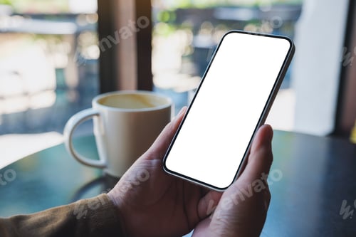 Preview: Mockup image of hands holding mobile phone with blank desktop screen with coffee cup on the table