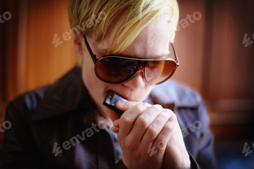 Preview: Making mellow music. Attractive young guy in urban wear playing the harmonica.