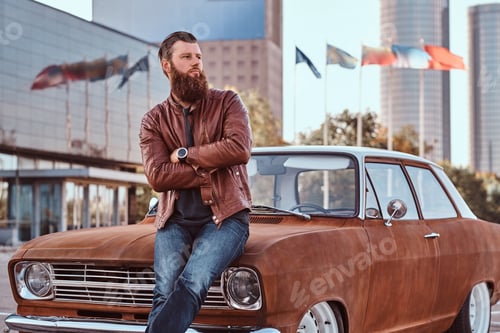 Preview: Bearded male dressed in brown leather jacket and boots with tuned retro car