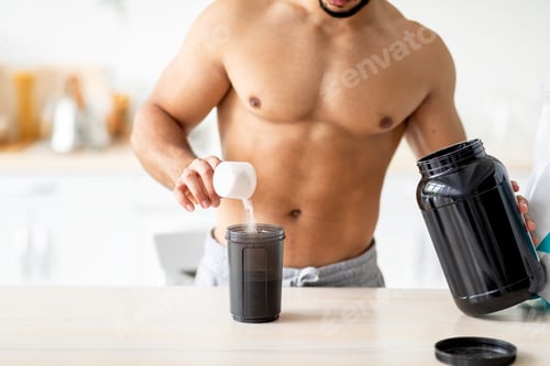 Preview: Cropped view of sexy shirtless young man with nakes chest making protein shake at kitchen, closeup