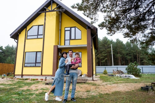 Preview: Happy family in the yard of an unfinished house - purchase of a cottage