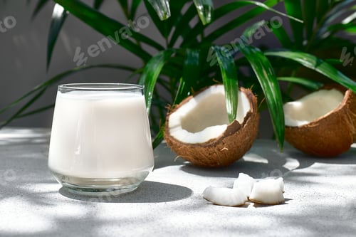 Preview: Coconut milk in glass and half of coconut on palm leaf background.