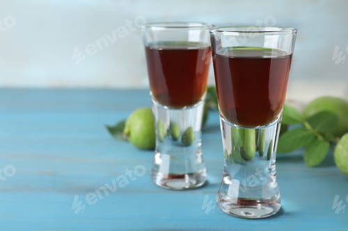 Preview: Delicious liqueur and green walnuts on light blue wooden table, closeup. Space for text