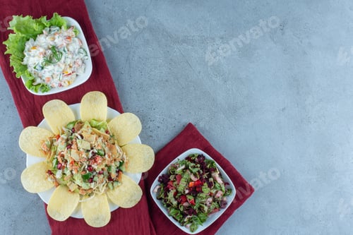 Preview: Line-up of various salads garnished with lettuce leaf and potato chips on marble background