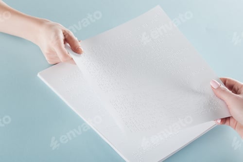 Preview: cropped view of young women holding paper with braille text isolated on blue