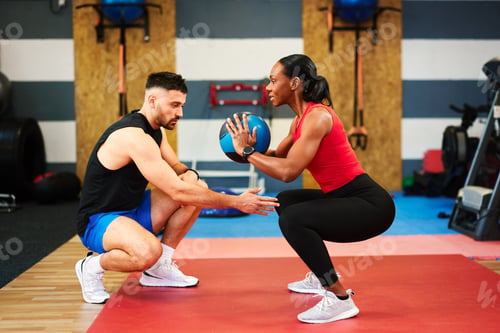 Preview: Determined woman performing squats with medicine ball under supervision of personal trainer