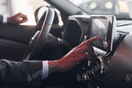 Preview: Using front control panel. Young african american businessman in black suit is in the automobile