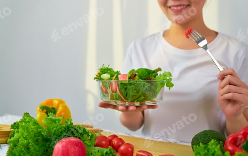 Preview: Woman hands holding salad bowl with eating tomato and various green leafy vegetables on the table at