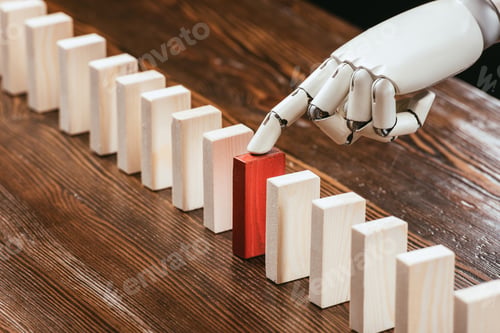 Preview: selective focus of robotic hand picking red wooden brick from row of blocks on desk