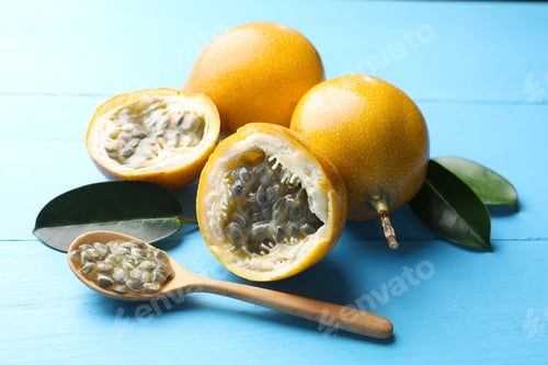Preview: Ripe passion fruits, green leaves and seeds on light blue wooden table, closeup