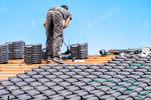 Preview: workman installs a fired ceramic tile on the roof of family house