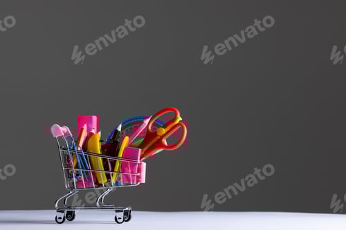 Visualização: Vista de perto do carrinho de compras em miniatura com materiais escolares e espaço de cópia em fundo cinza