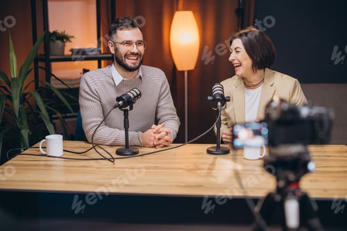 Preview: Cheerful podcast hosts laughing while recording inside sleek, contemporary studio