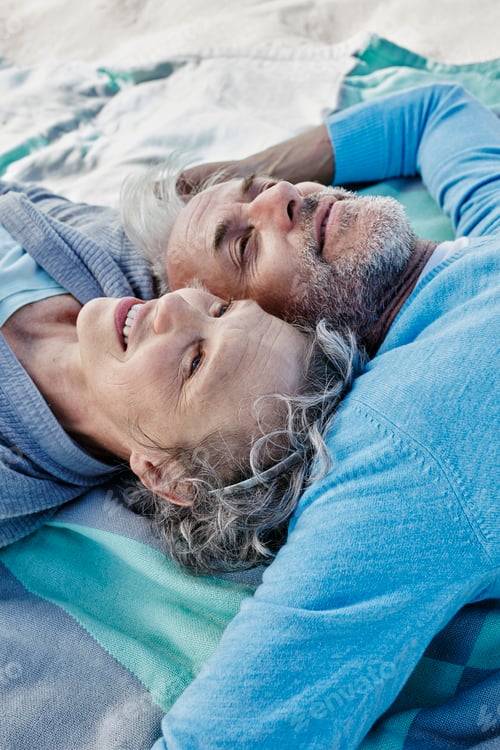 Preview: Happy couple lying head to head on blanket on the beach