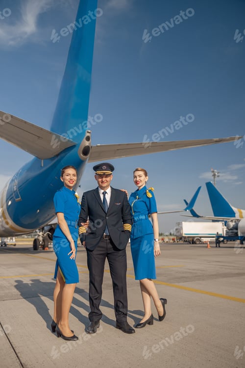 Preview: Full length shot of cheerful pilot and two pretty stewardesses standing together