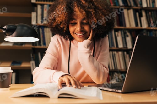 Preview: Smiling girl sitting at desk and reading in library
