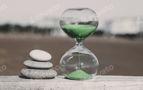 Preview: Pyramid of three stones nearby and an hourglass with green sand. Vacation time concept