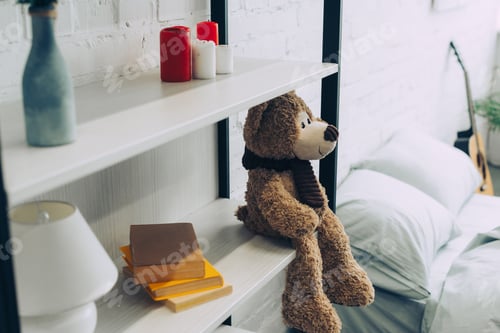 Preview: high angle view of teddy bear sitting on shelves with books and candles at home